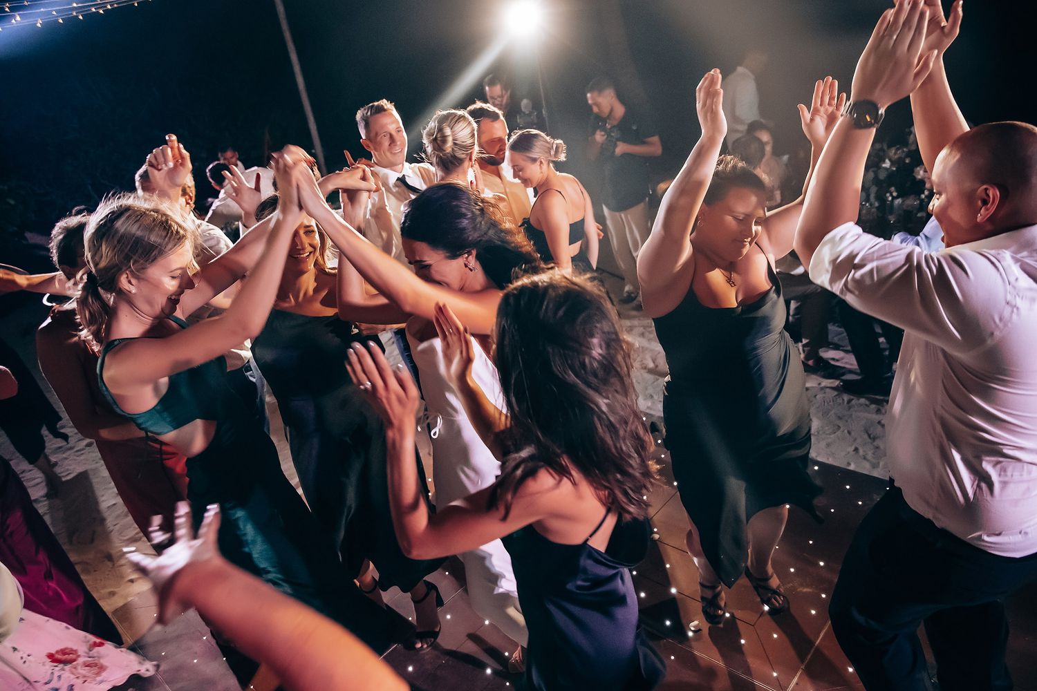 Energetic crowd dancing and celebrating at a dimly lit indoor reception party.