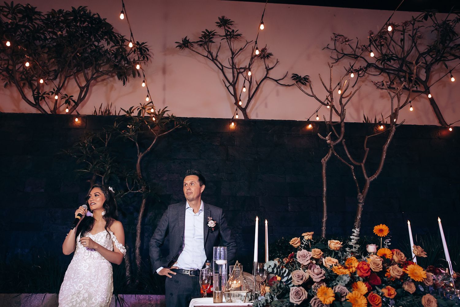 Evening outdoor reception with string lights and autumn decor under night sky.