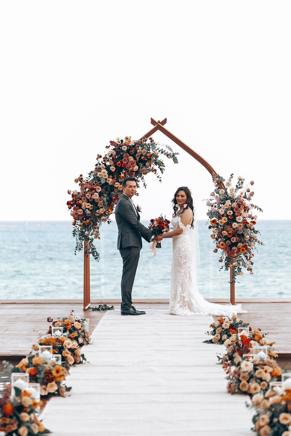 Beachfront wedding ceremony with coral and peach floral arrangements lining the aisle.