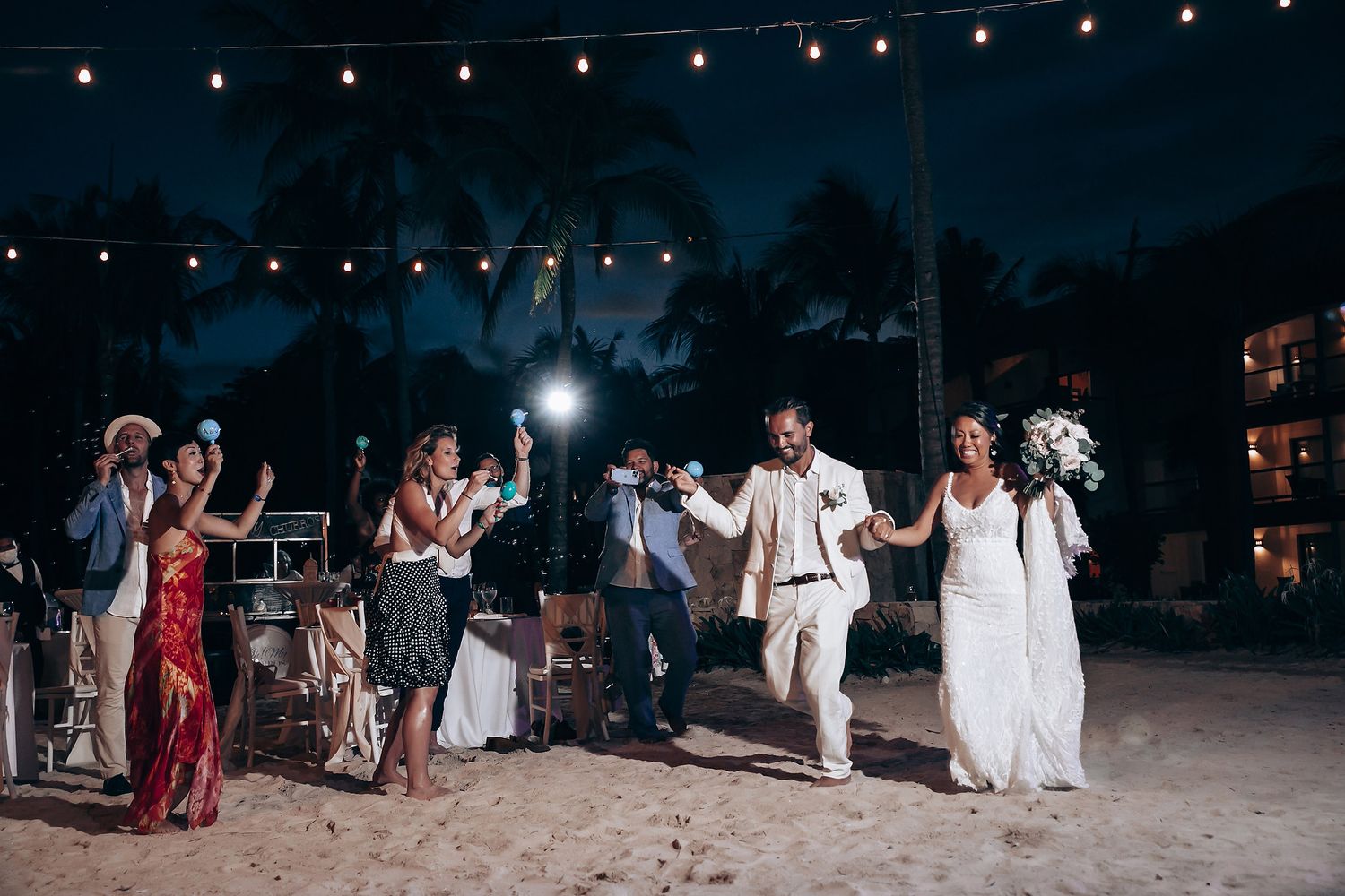 Wedding guests dance and celebrate under twinkling string lights at an outdoor evening reception.