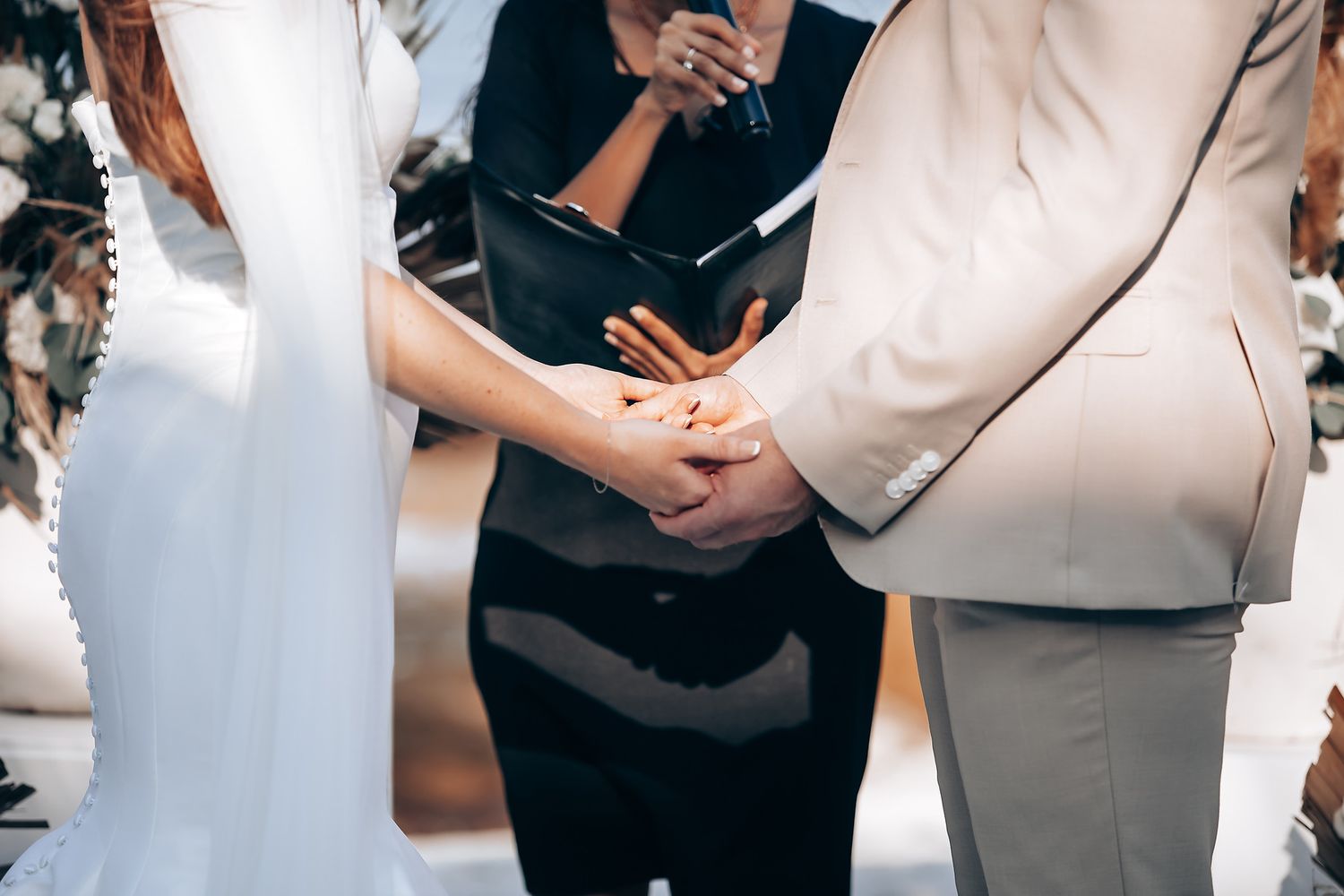 Close-up view of hands during an intimate wedding ceremony with an officiant in beige attire.