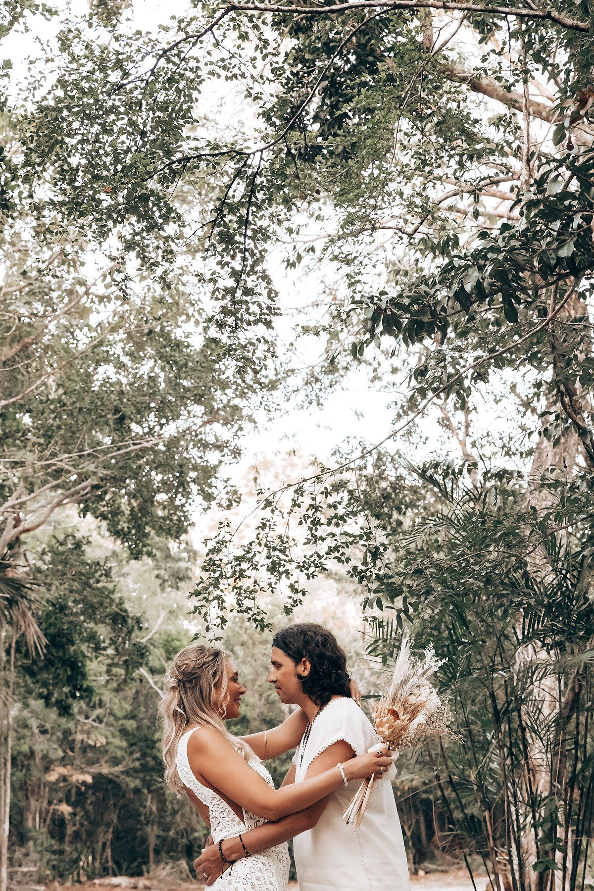 Two people share an intimate moment while dancing together in a sunlit wooded area outdoors.