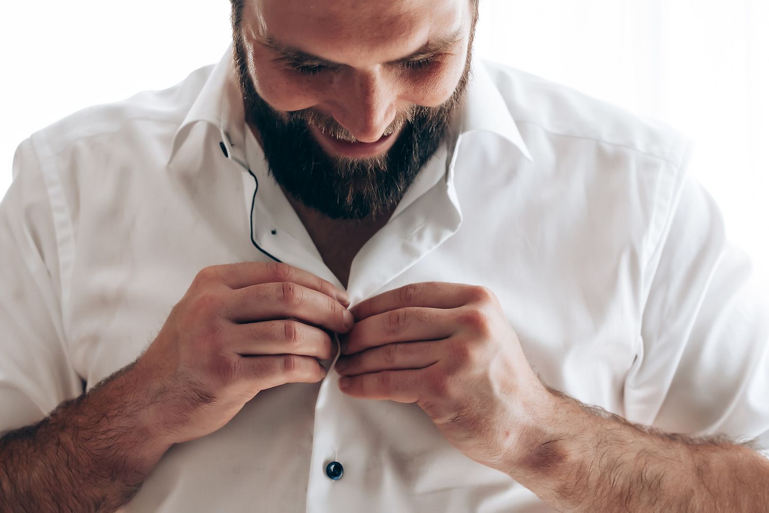 A person in a white button-up shirt sniffing and examining coffee beans in their hands.