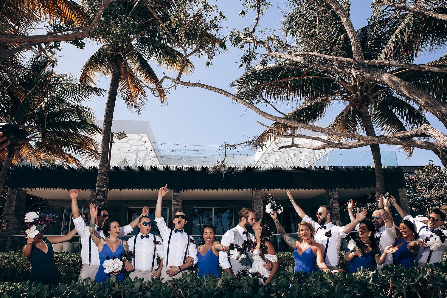 Wedding guests seated in rows under swaying palm trees at a beachside venue.