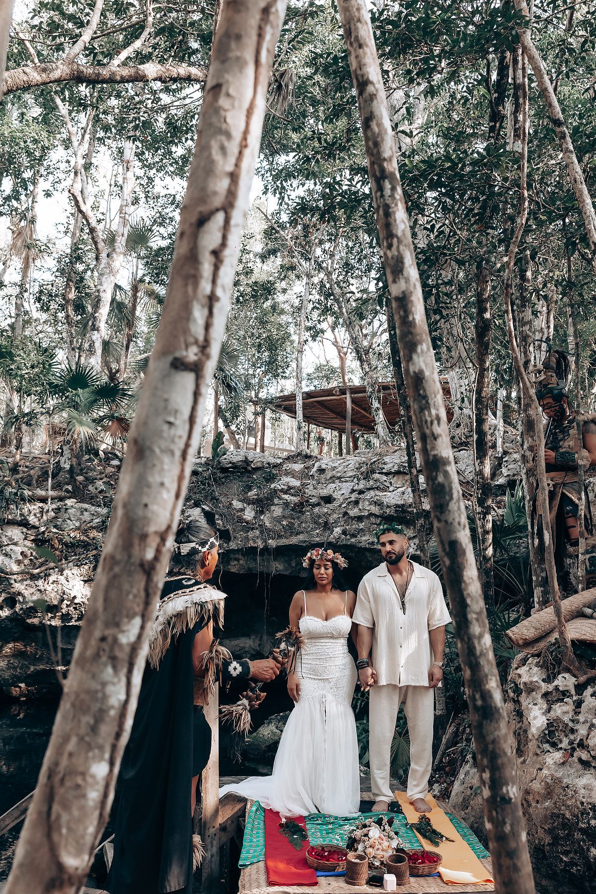 Sacred ceremony takes place on red carpet among tall trees near a cenote.
