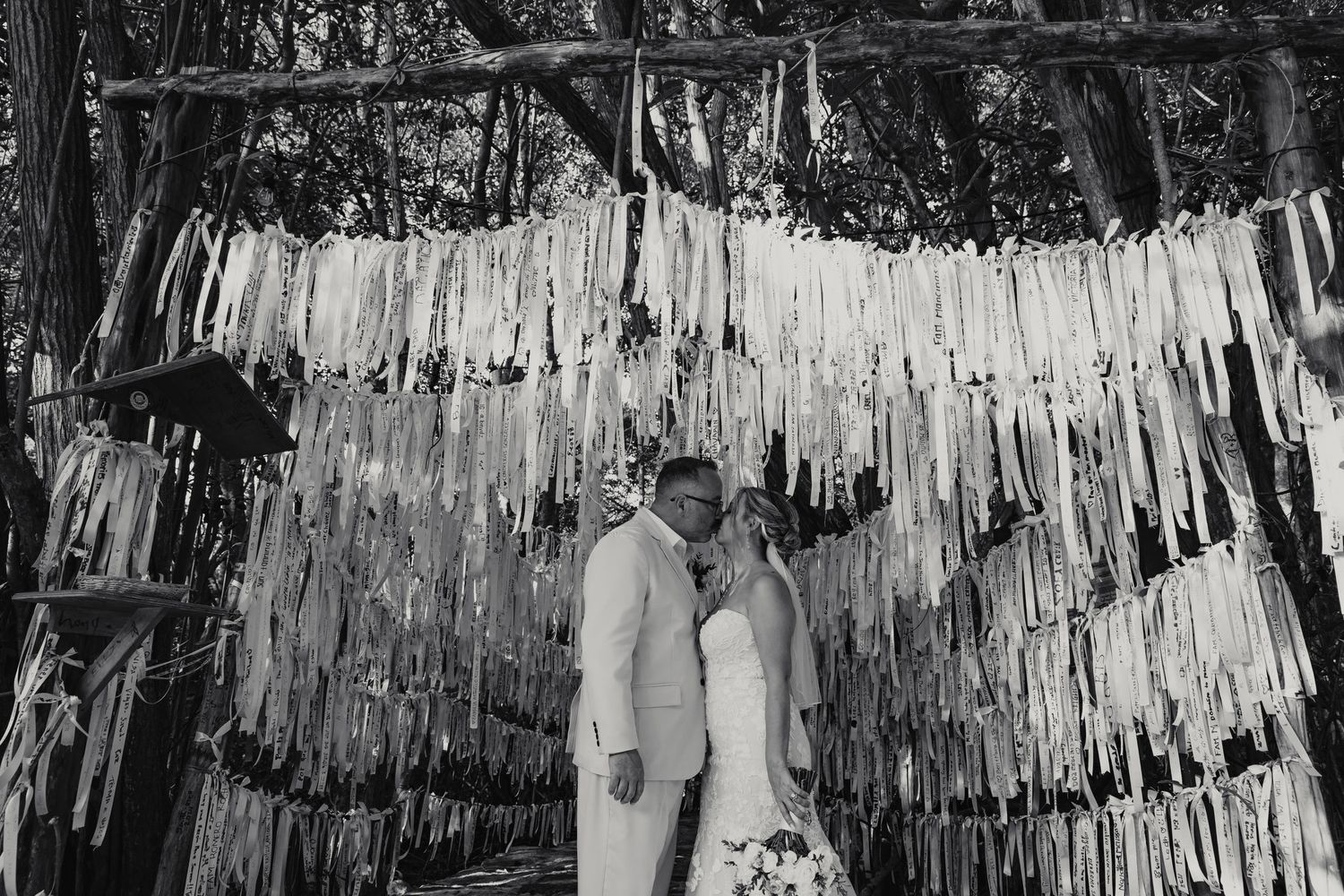 Bride and groom share a kiss beneath decorative ribbon curtain backdrop in black and white.