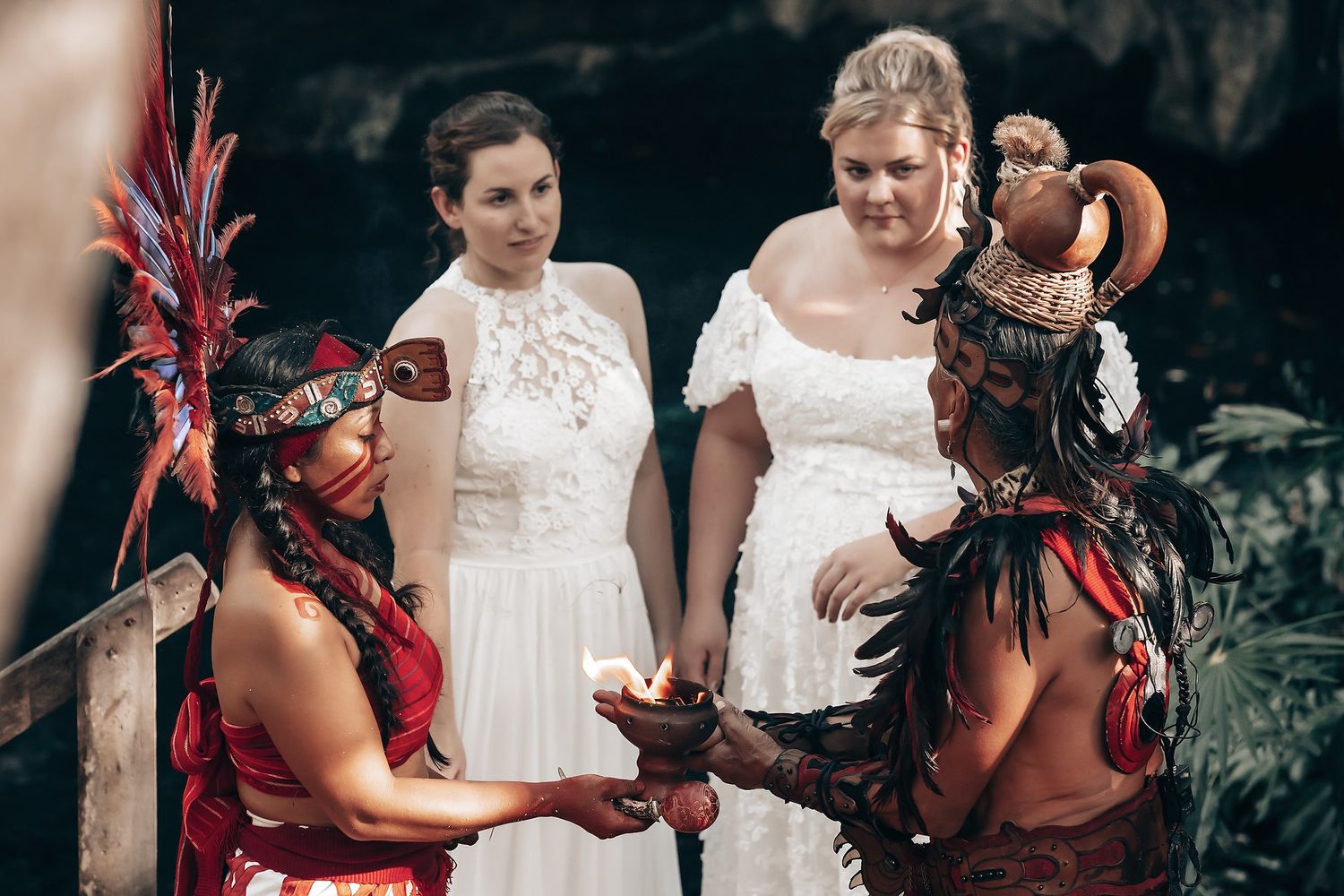 Three people, two women and one man, wearing traditional ceremonial clothing in a natural setting.