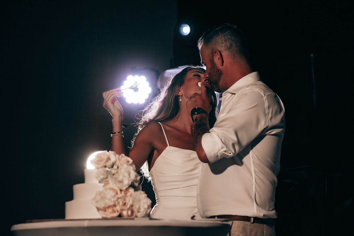 A bride and groom cut their wedding cake together, surrounded by candles and flowers.