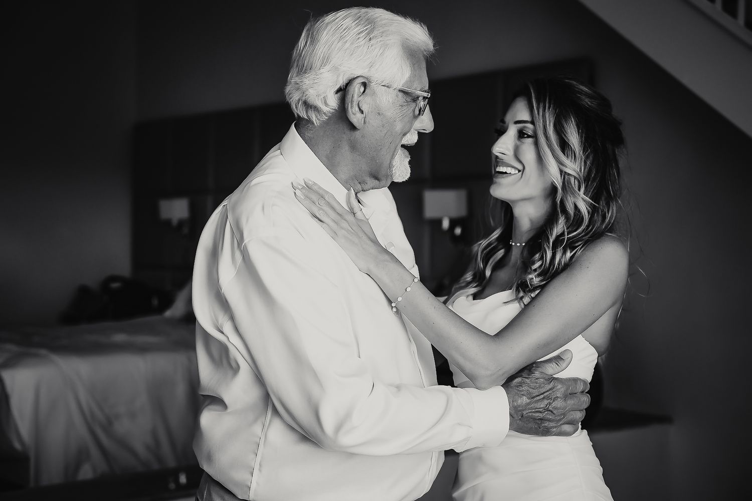 An older man and a younger woman embrace in a bedroom.