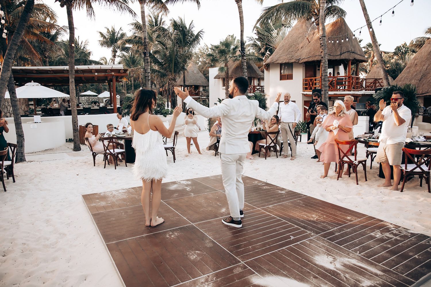 Beach wedding reception setup with rustic wooden tables and thatched roof palapas.