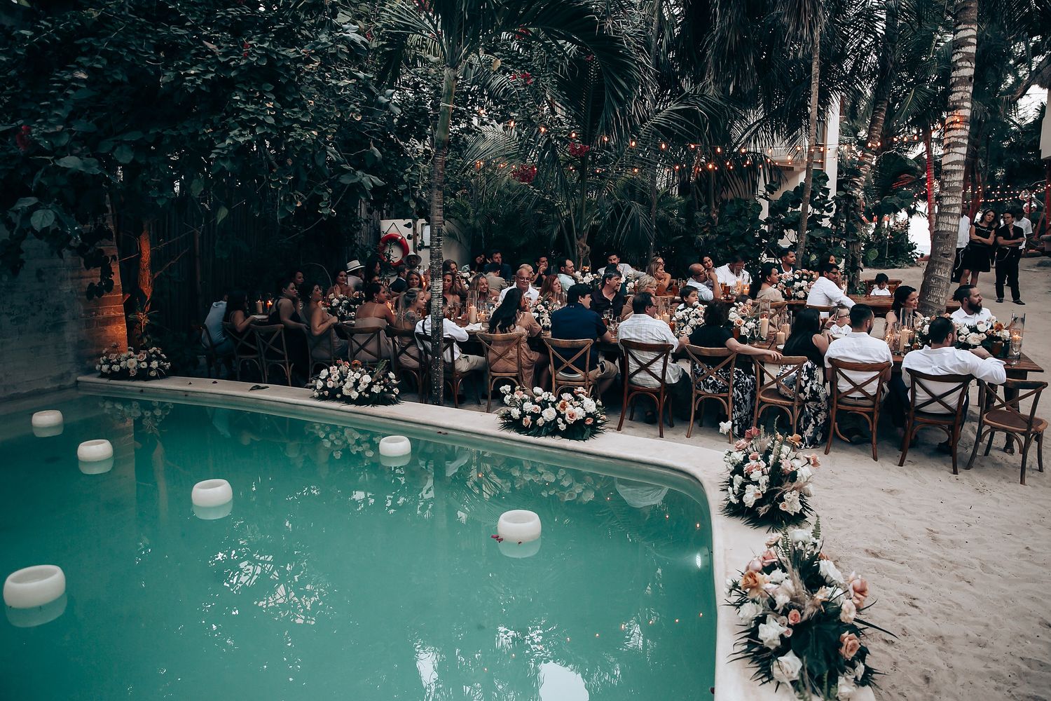 Poolside wedding reception setup with turquoise water and floral decorations.