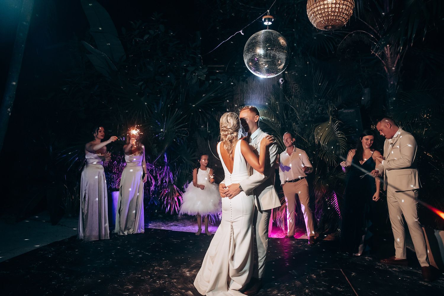 Wedding reception dance floor illuminated by disco balls and purple lighting.