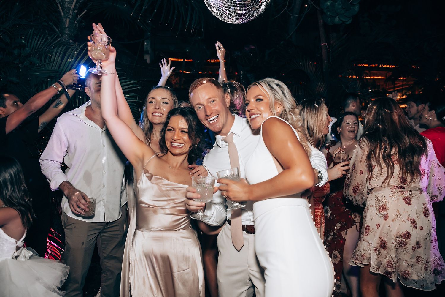 Wedding reception dance party with disco ball and energetic crowd on dance floor.