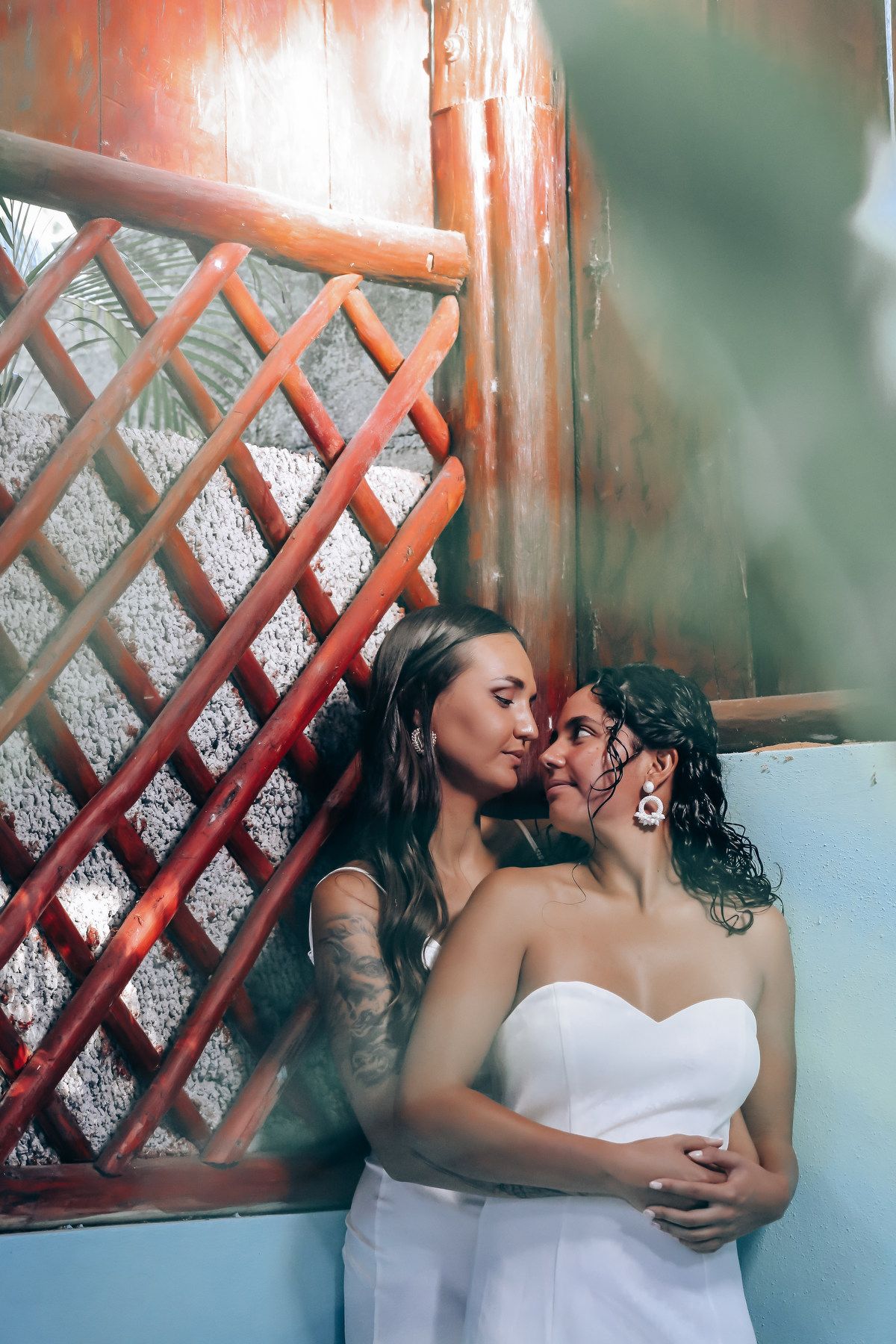 Two people in white outfits share an intimate moment against a wooden lattice wall.