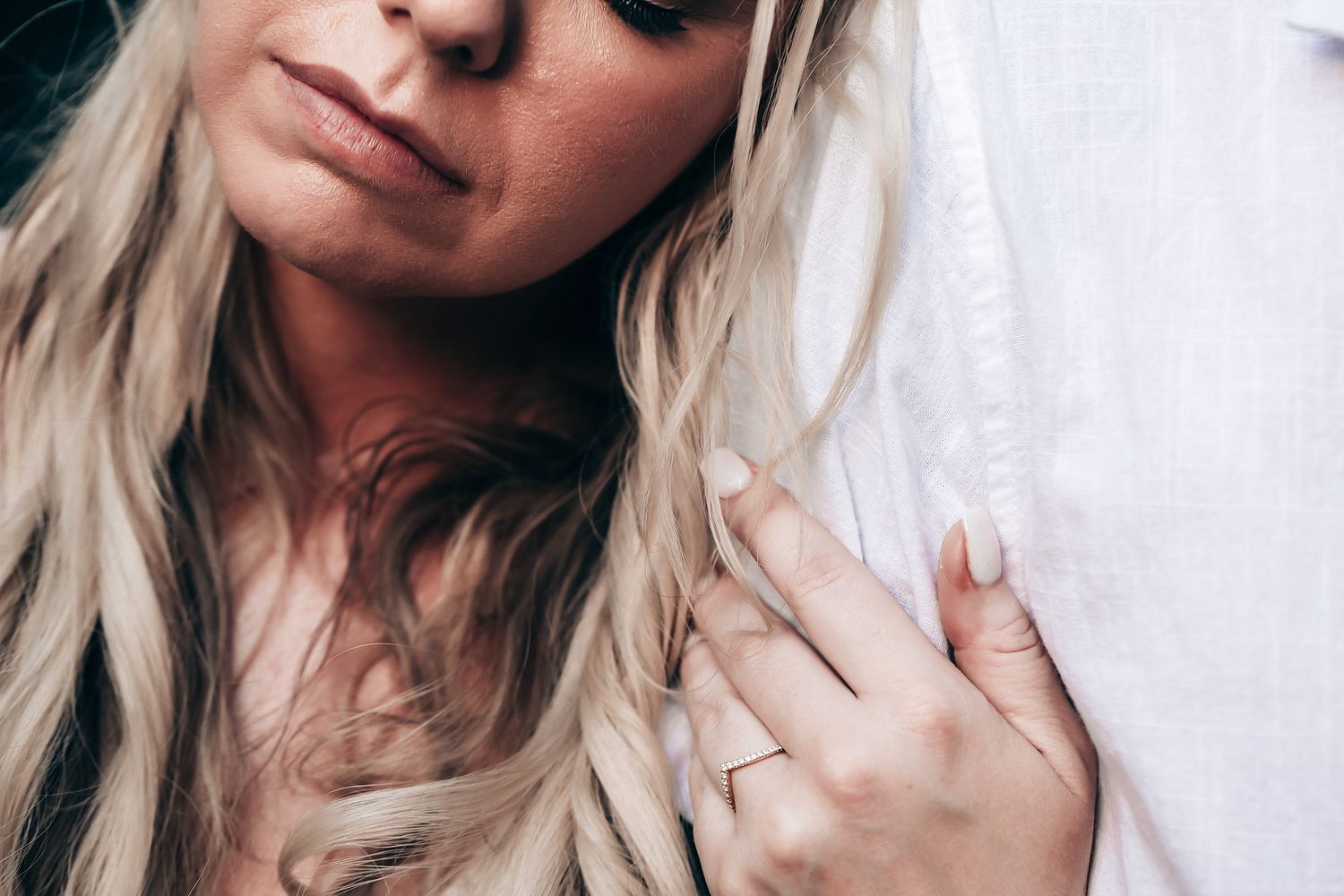 Close up shot of blonde hair and white fabric with an engagement ring visible.