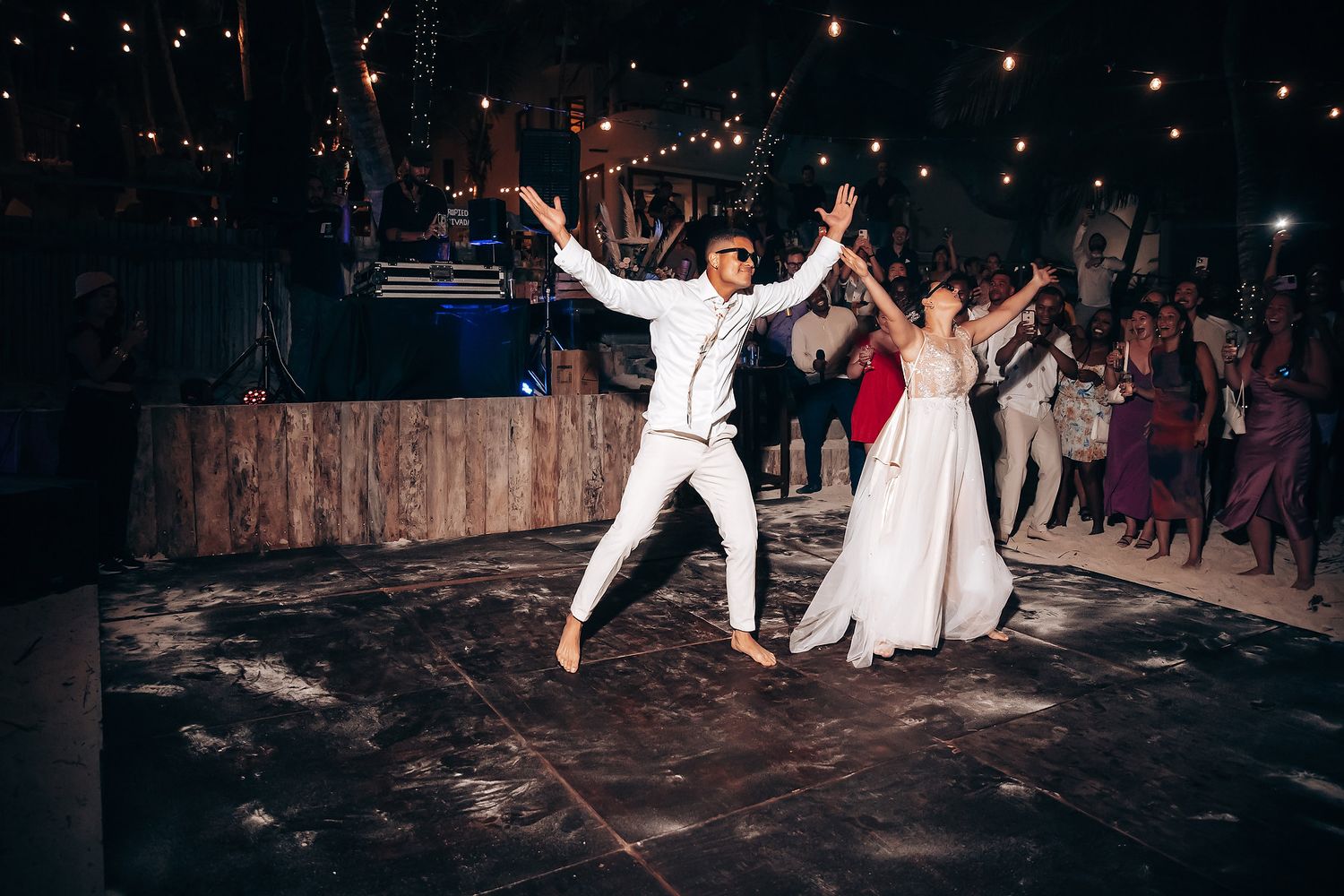 Wedding reception dance party at night with string lights and energetic dancing.