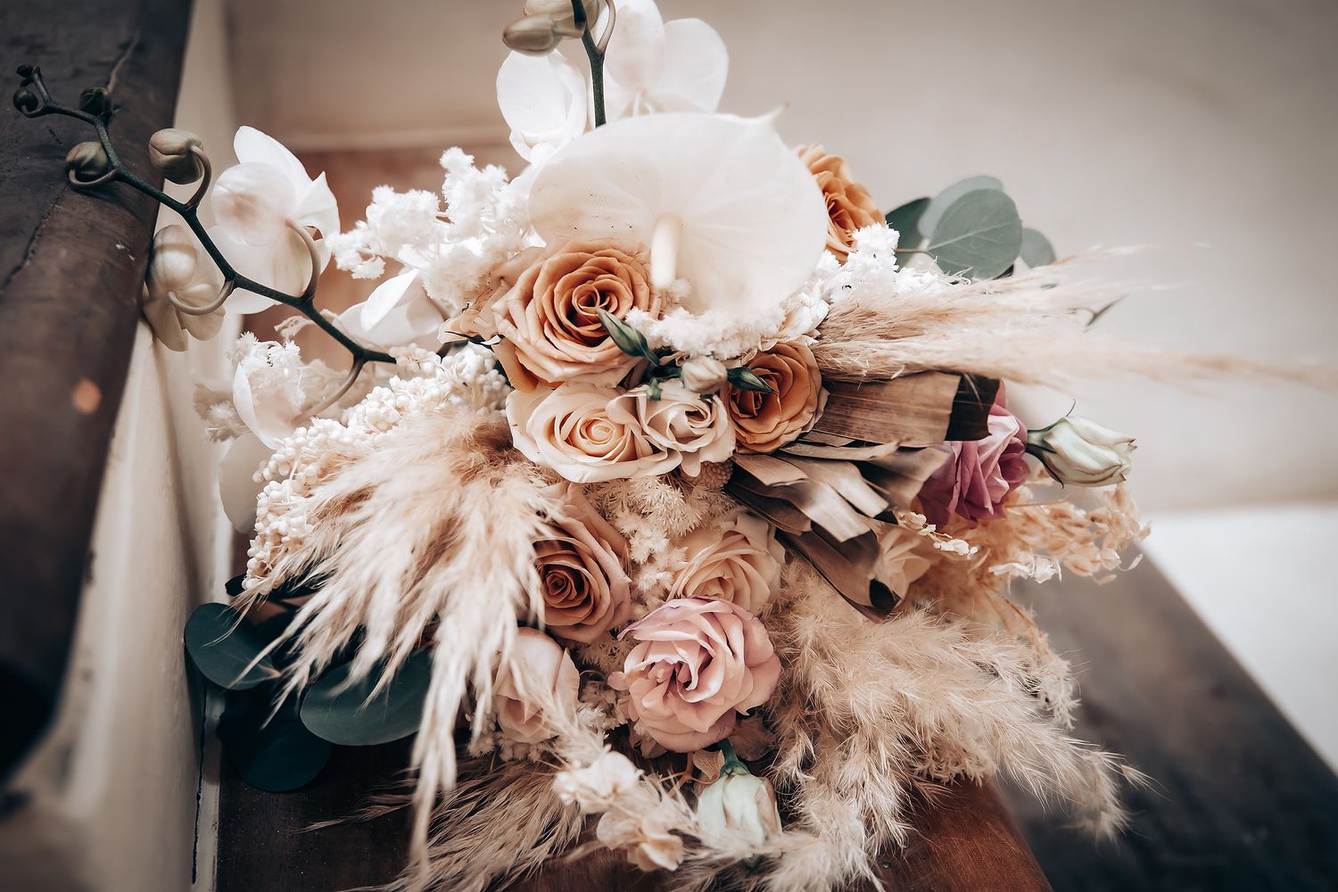 Delicate peach and blush colored floral arrangement with roses and pampas grass against a soft neutral background.
