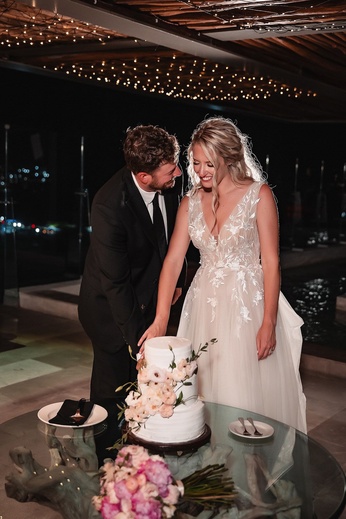 Couple cutting their wedding cake under string lights at an evening reception.