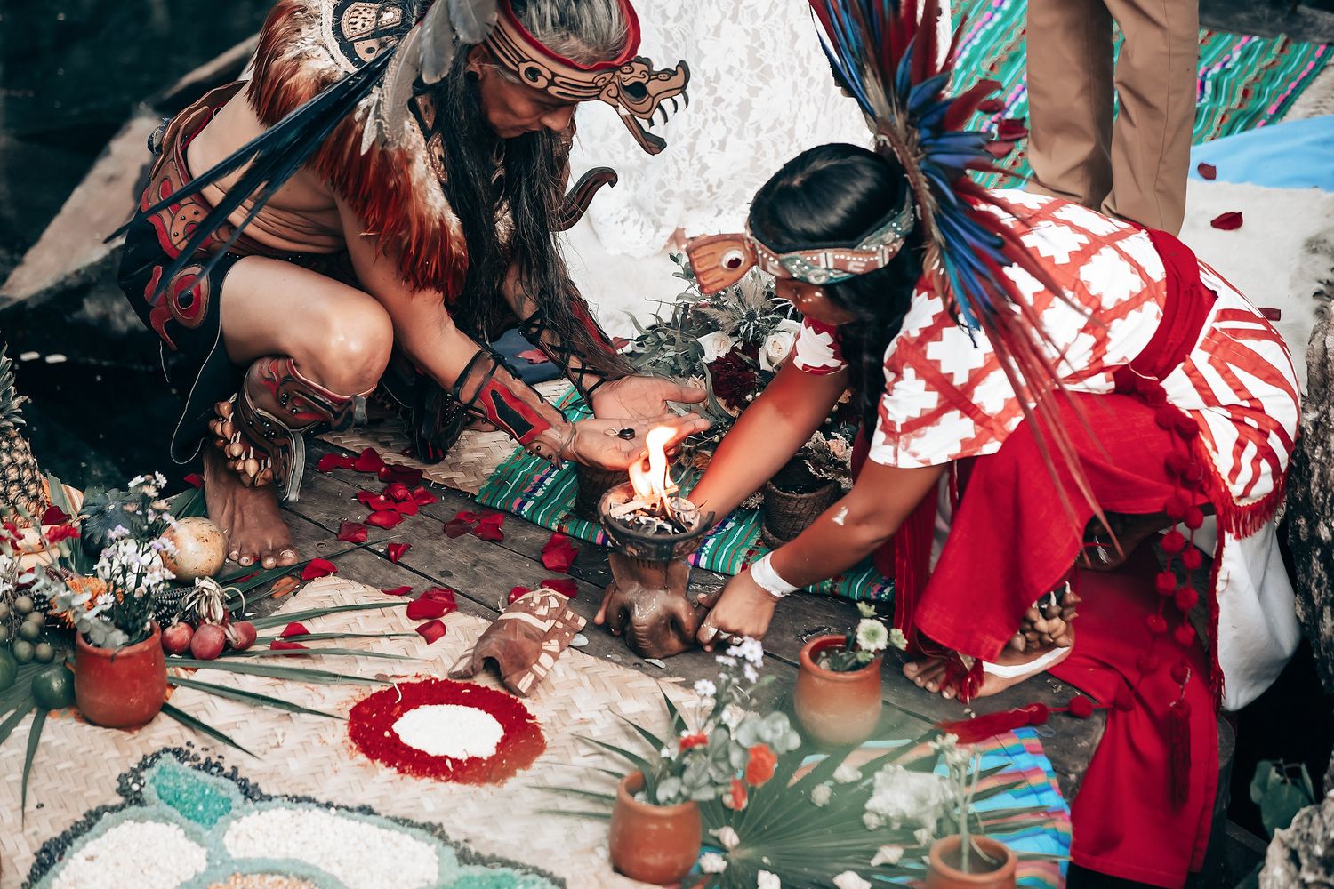 Ritual ceremony items arranged on ground with red and white textiles.