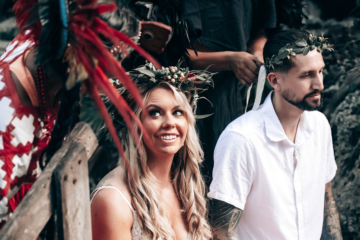 A wedding couple and their party celebrate outdoors with burgundy floral arrangements and white attire.