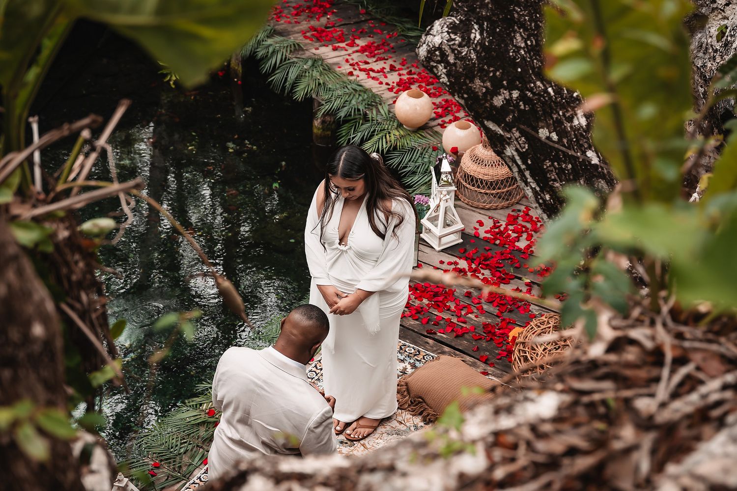 Intimate proposal moment on decorated platform over turquoise water in natural cave setting.