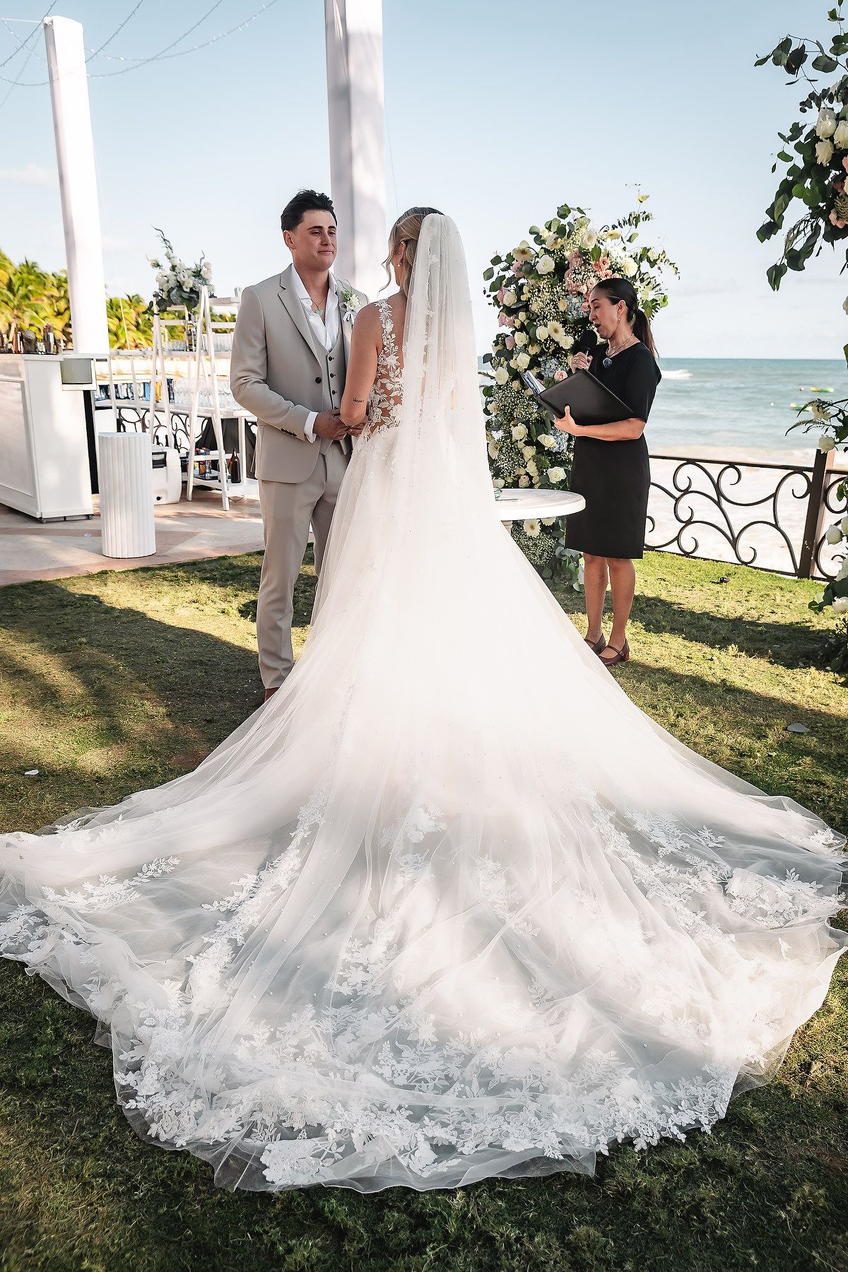 A flowing white wedding dress train spreads beautifully across green grass by the ocean.