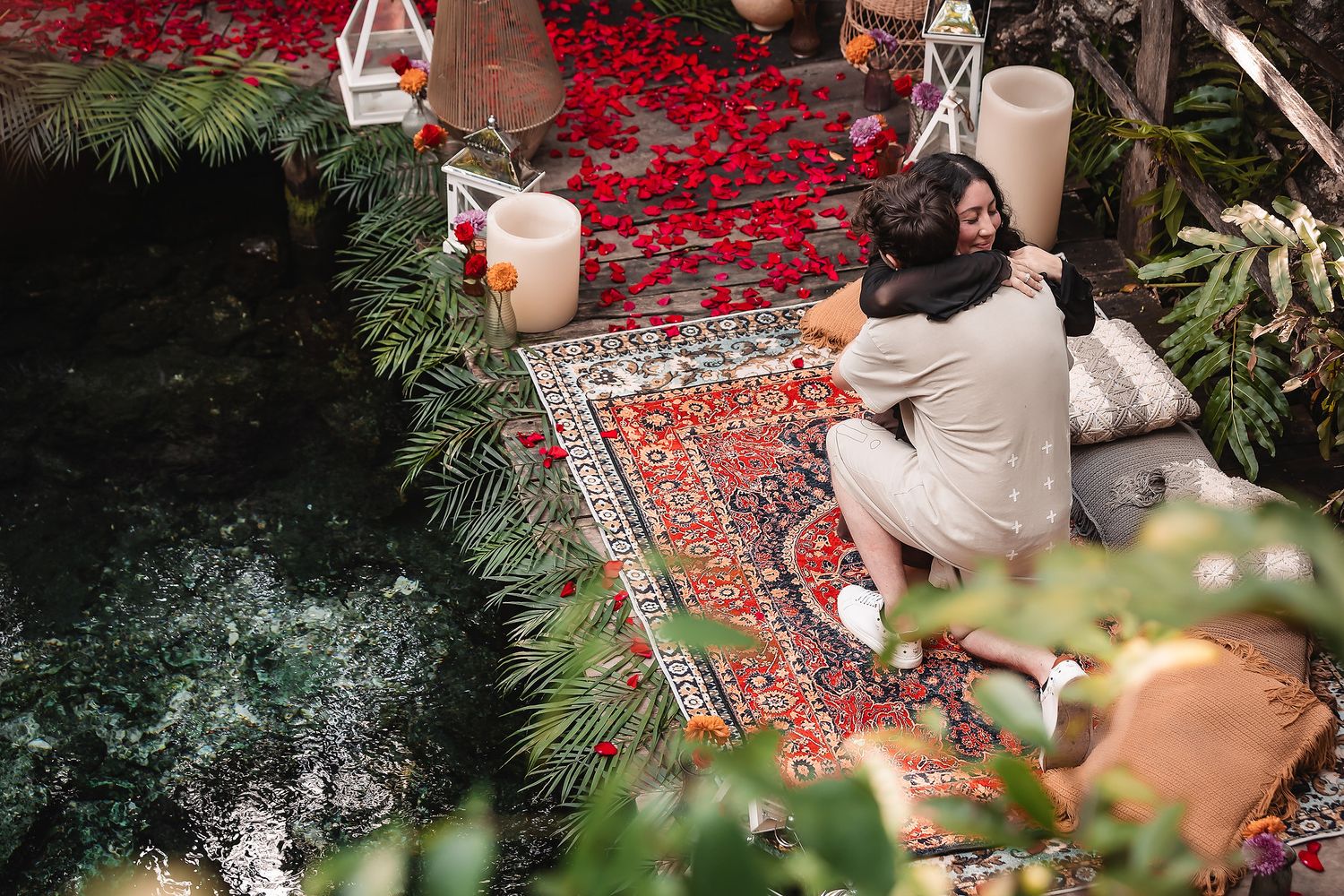 Romantic cenote setting with Persian rug and white lanterns among tropical foliage.