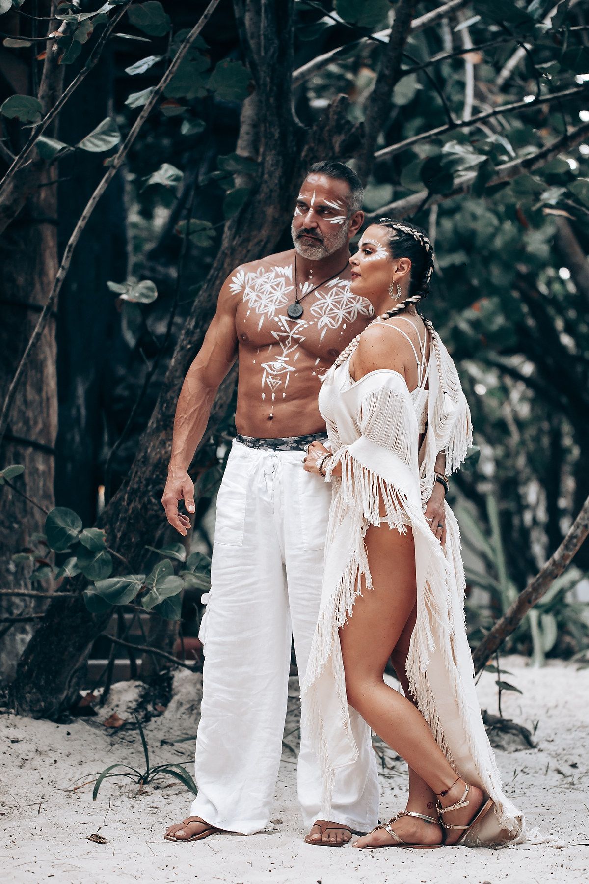 A romantic beach photoshoot featuring white bohemian outfits and tribal body paint against a tropical backdrop.