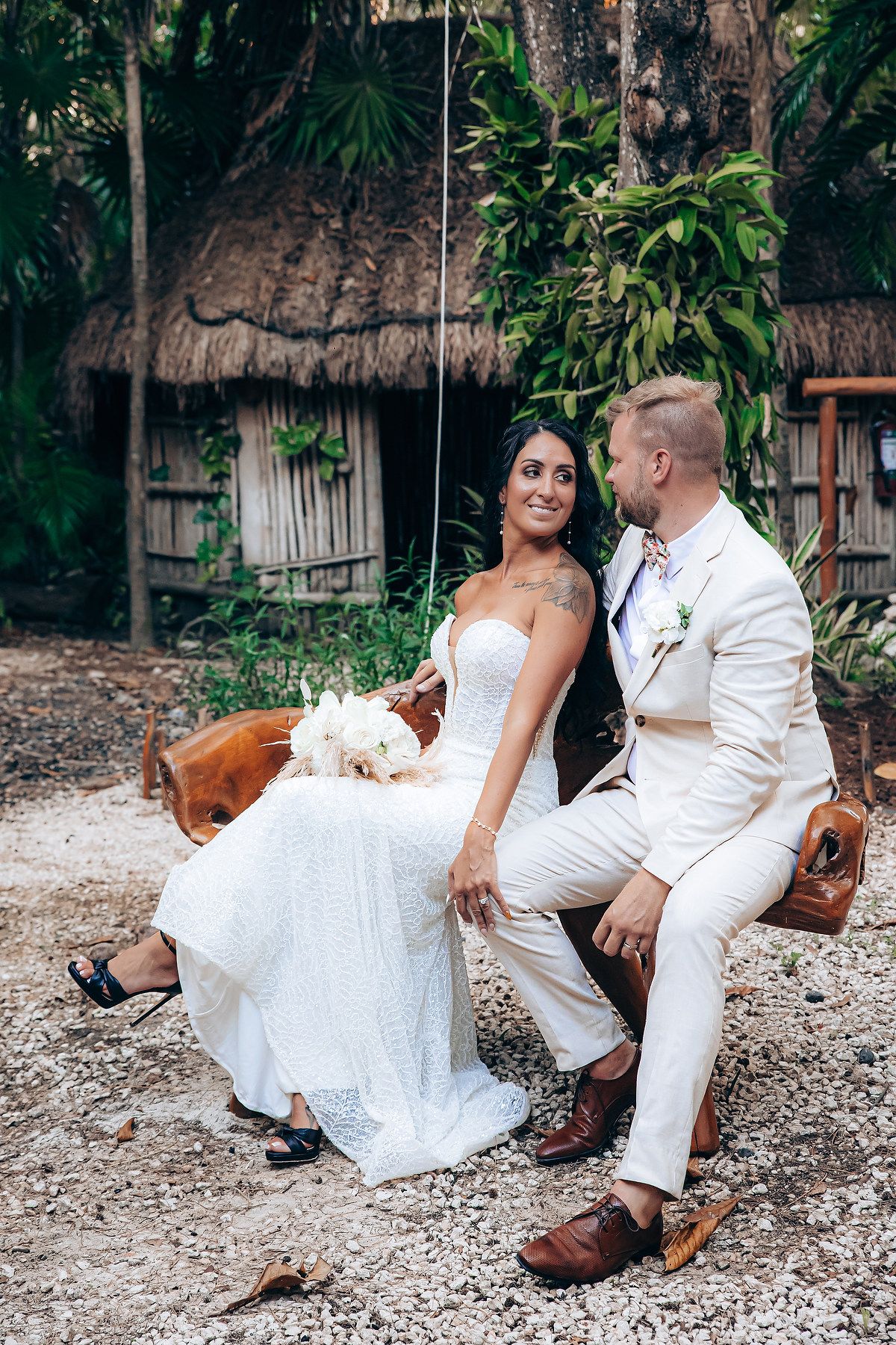 Newlyweds relaxing on vintage leather chairs in tropical garden setting.