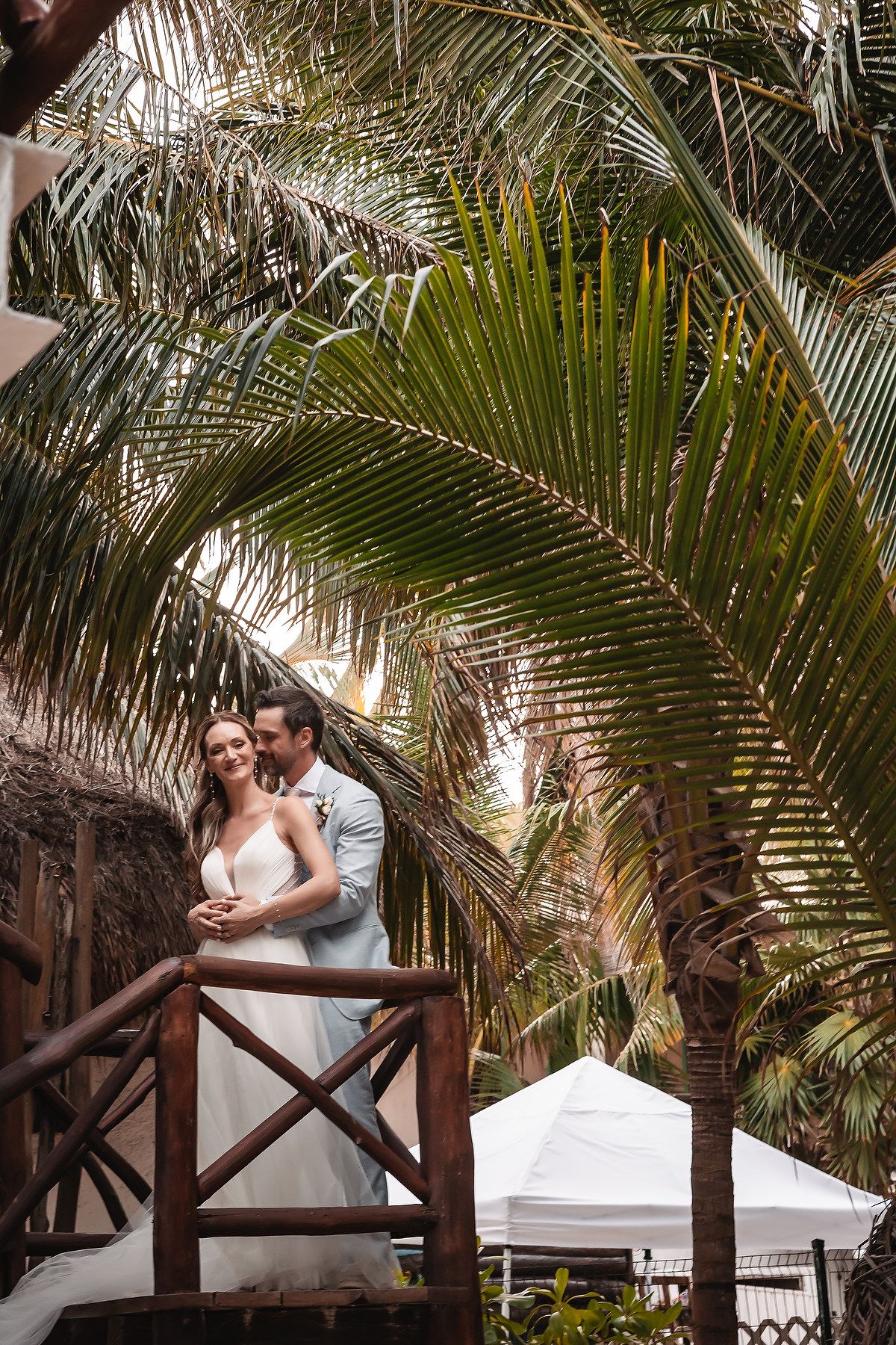 Tropical wedding photography with palm trees framing the couple against wooden railings.
