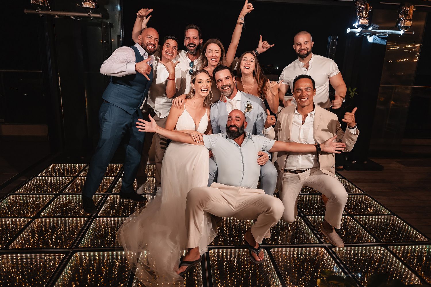 Wedding party members posing playfully together on illuminated dance floor during reception.