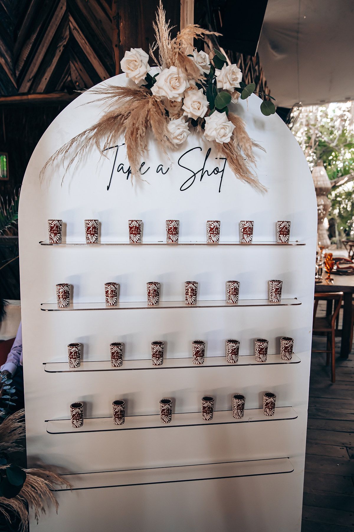 White wedding display board with metallic cups arranged in rows and decorated with dried flowers and text.