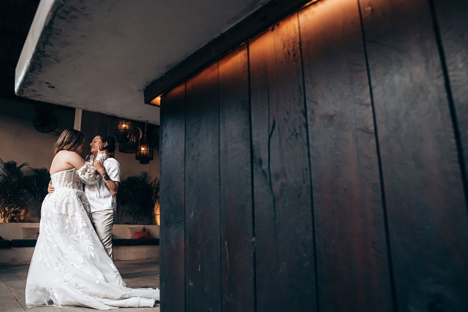 Couple sits on dark wooden floor in modern indoor setting with dramatic lighting.