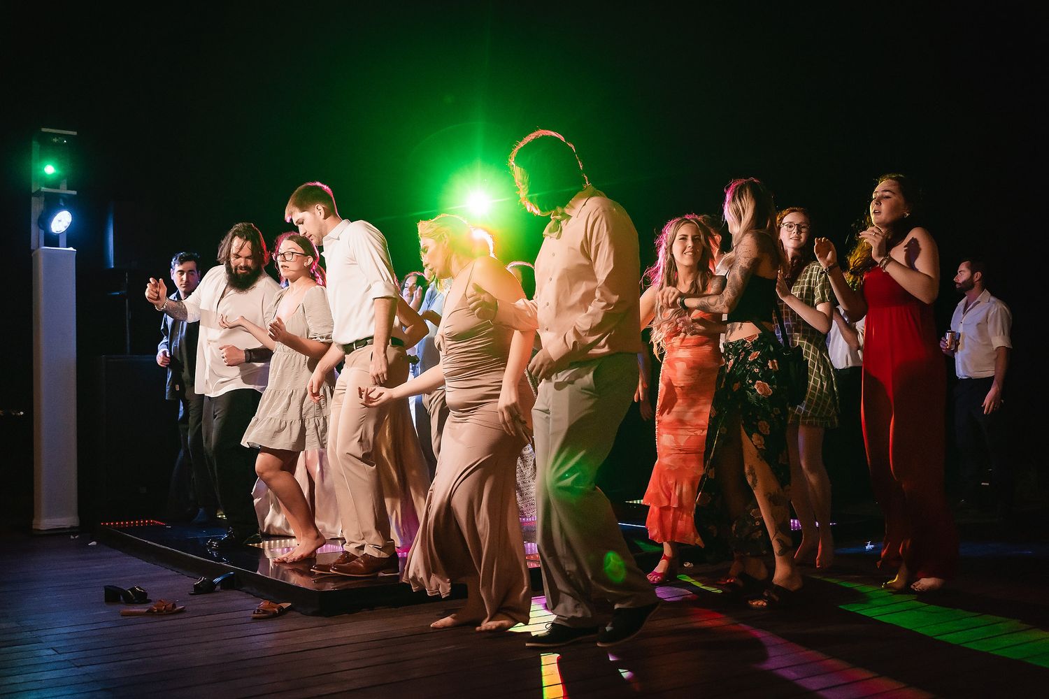 Wedding reception dance floor illuminated with green lighting as guests dance in the dark.