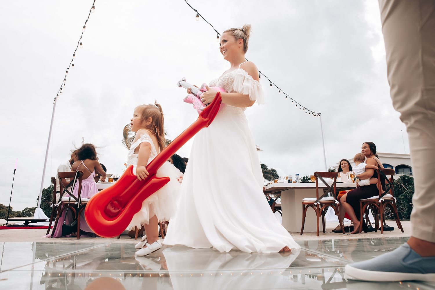 Wedding reception celebration with guests dancing under string lights and decorations.