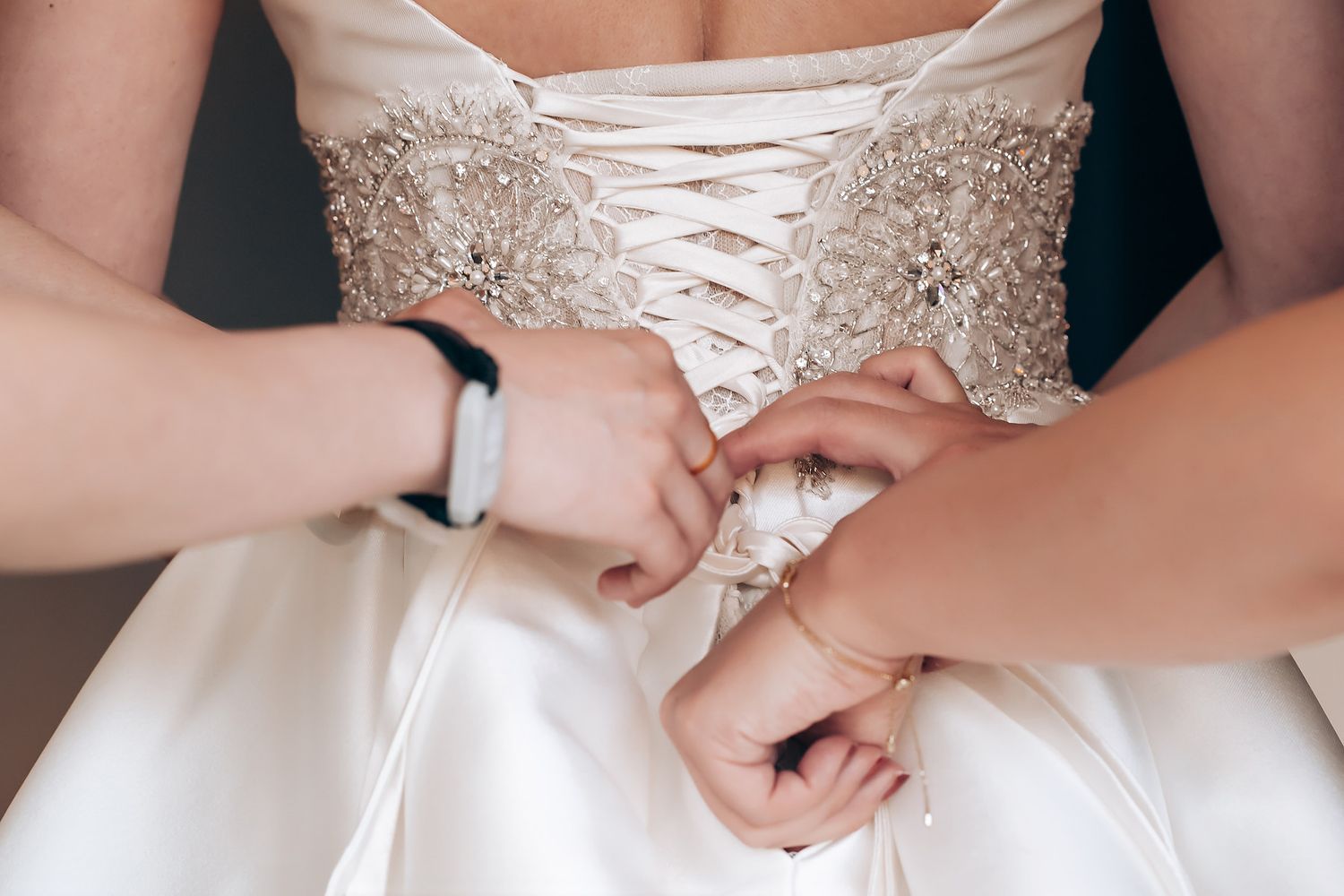 Close-up detail of white wedding dress corset lacing being adjusted.