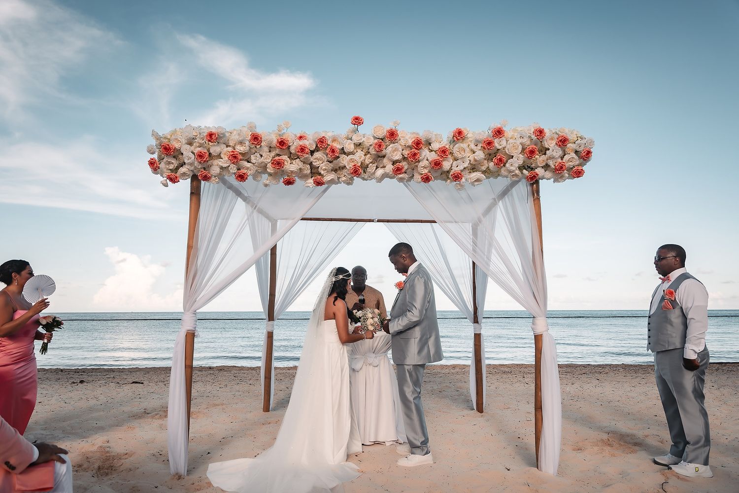 Panoramic view of a beachside wedding ceremony with white gazebo and floral arch decorations.