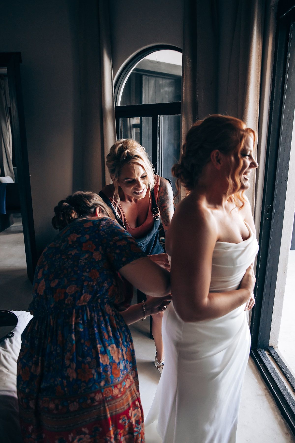 Wedding dress preparation moment in front of bright window.