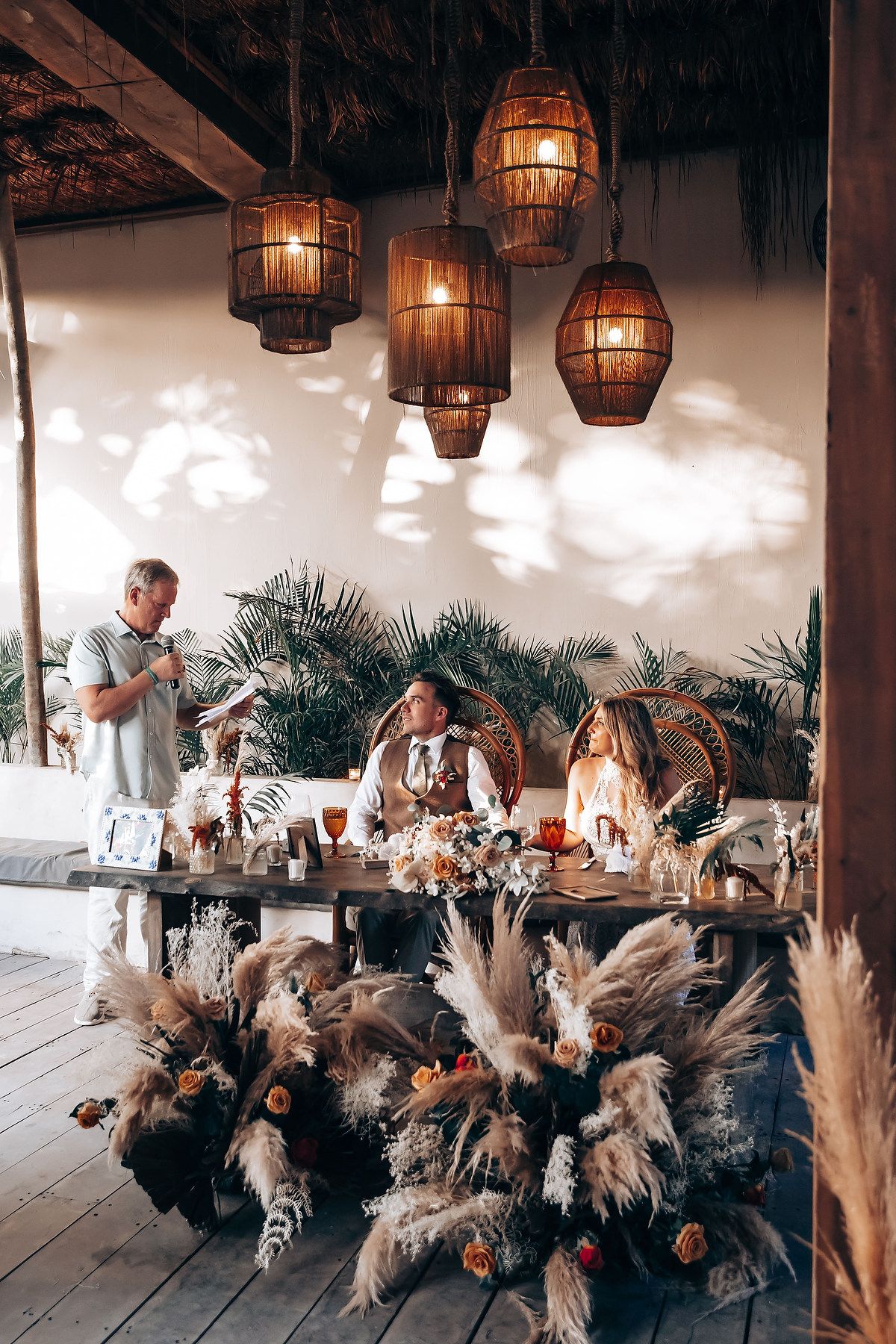 Wedding reception setup with hanging lanterns and bohemian dried flower arrangements.