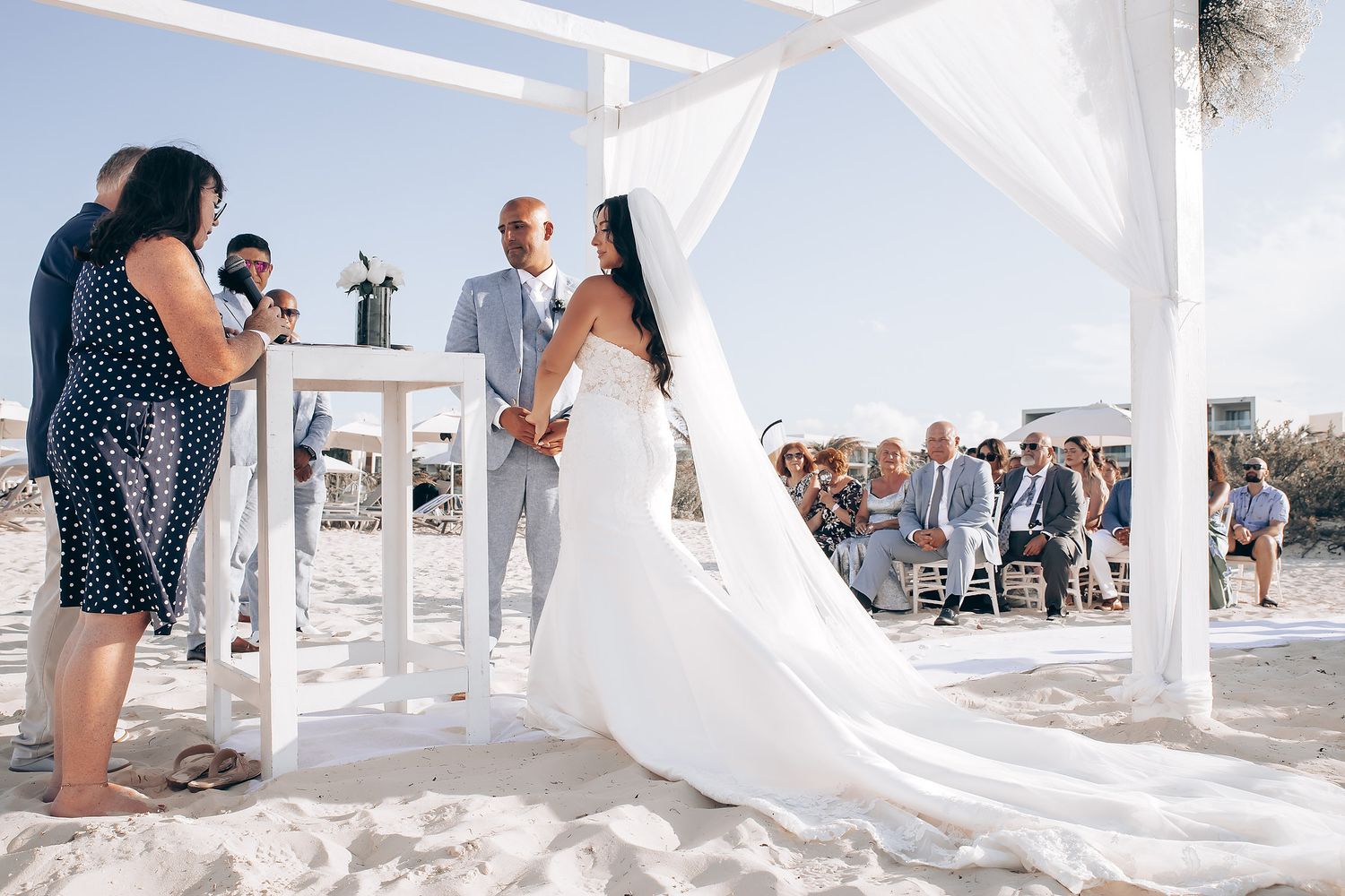 White wedding canopy blowing in the breeze on a sunny beach with turquoise ocean waters in the background.
