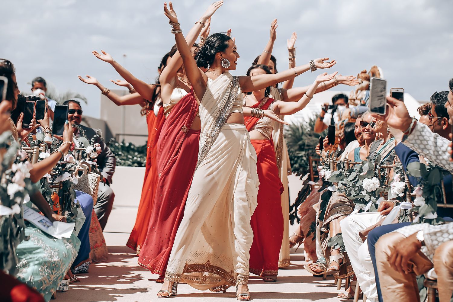 Celebratory dance performance at an outdoor wedding with guests in coral and cream attire.