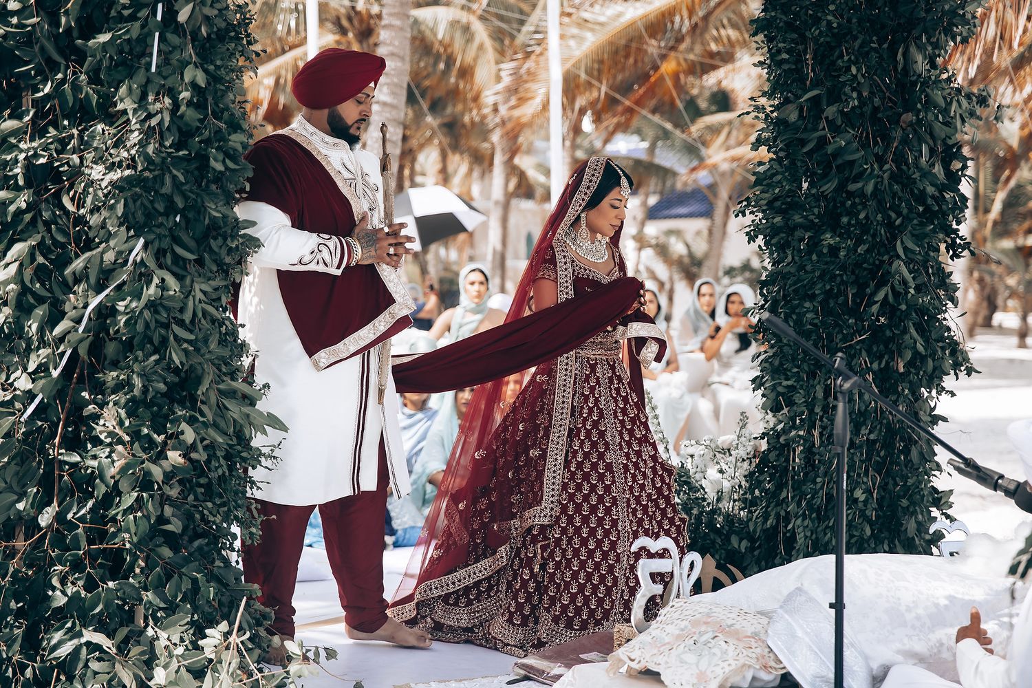 Traditional Indian wedding ceremony taking place under elegant floral mandap with hanging greenery.