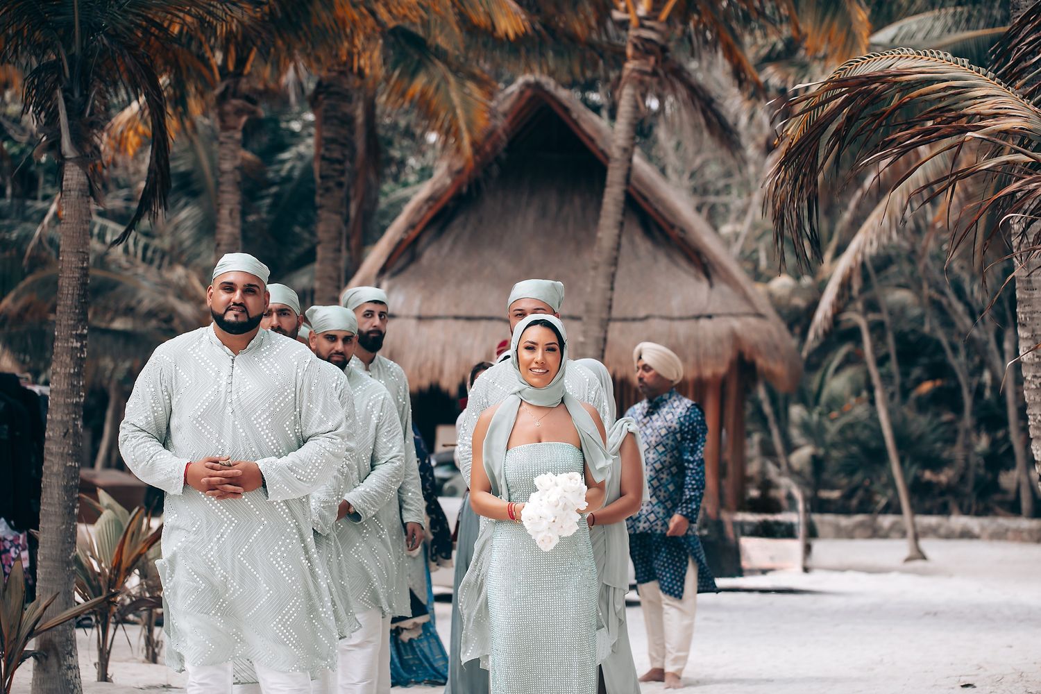 Beach wedding celebration with guests in white attire surrounded by palm trees.