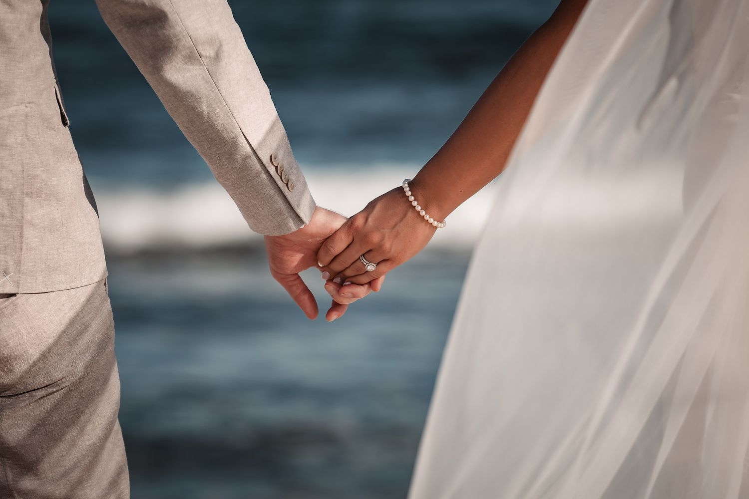 Elegant wedding couple walks hand in hand along a tropical beach at sunset.