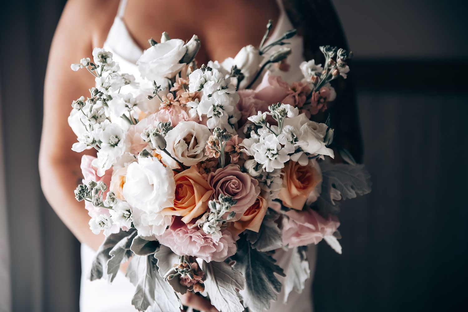 Beautiful bridal bouquet featuring white and pink flowers with delicate greenery against a light background.