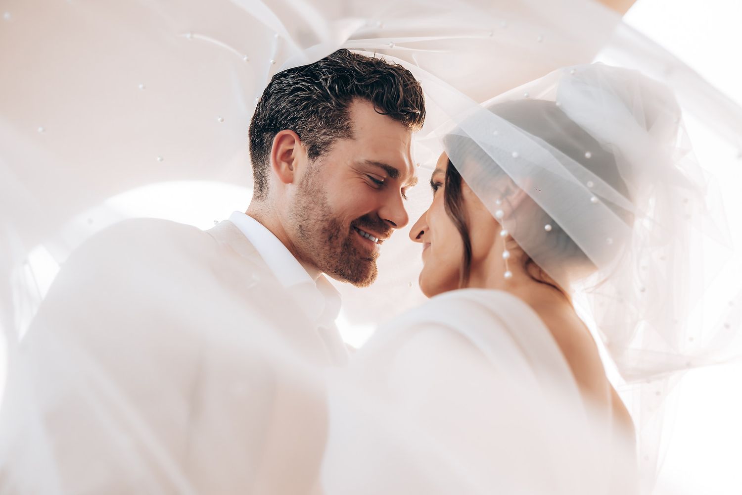 Tender moment between couple in white sharing a romantic embrace and gentle touch.