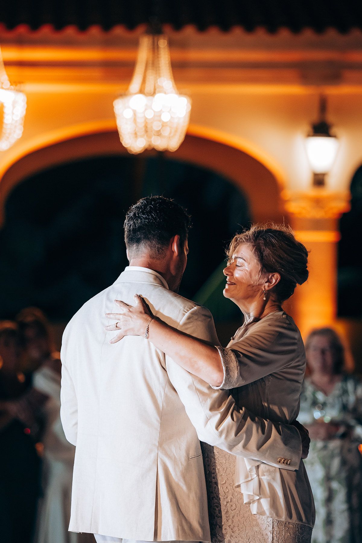 A couple shares a romantic dance moment at a wedding reception under warm amber lighting.