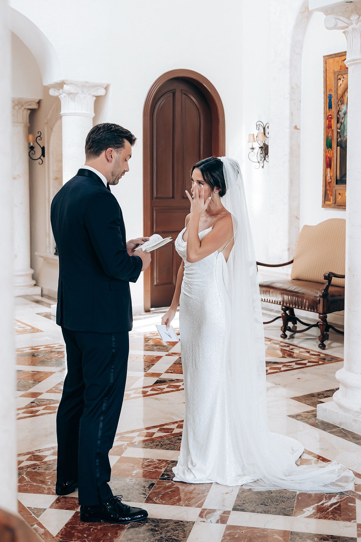 A couple shares an intimate moment between white columns in an elegant marble-floored hallway.