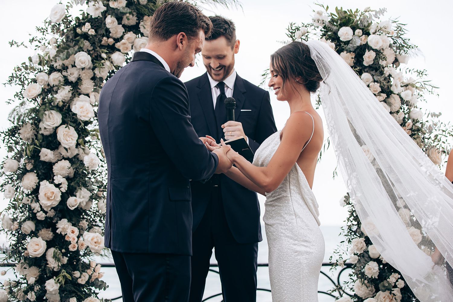 A joyful wedding celebration with a couple sharing an intimate moment under a white floral archway.