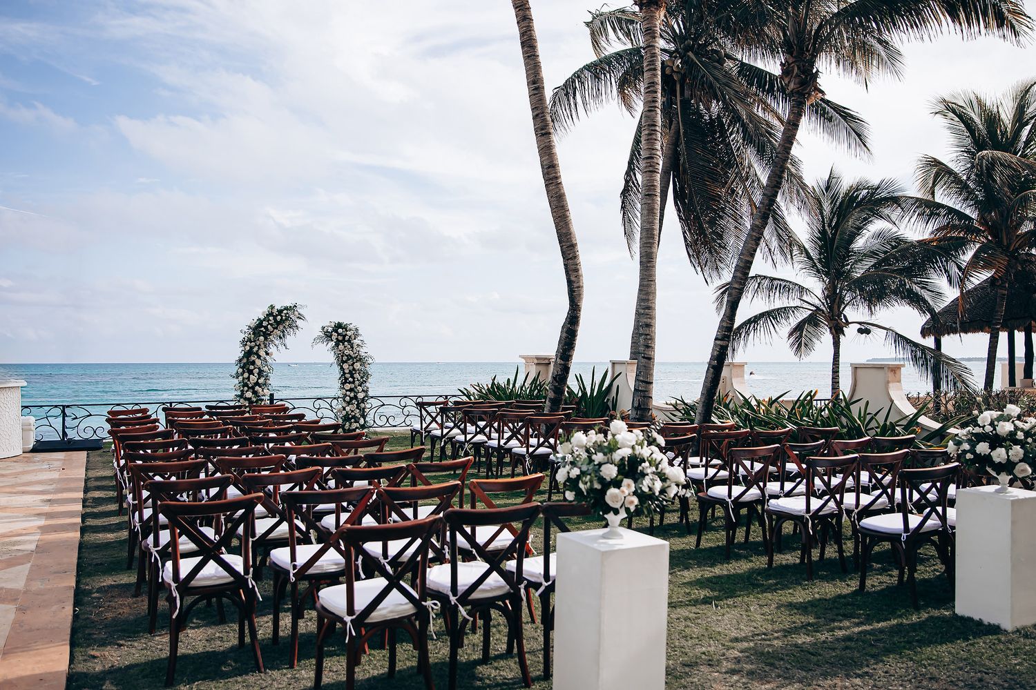 Wooden walkway with palm trees leads to a tropical beach wedding ceremony setup by the ocean.